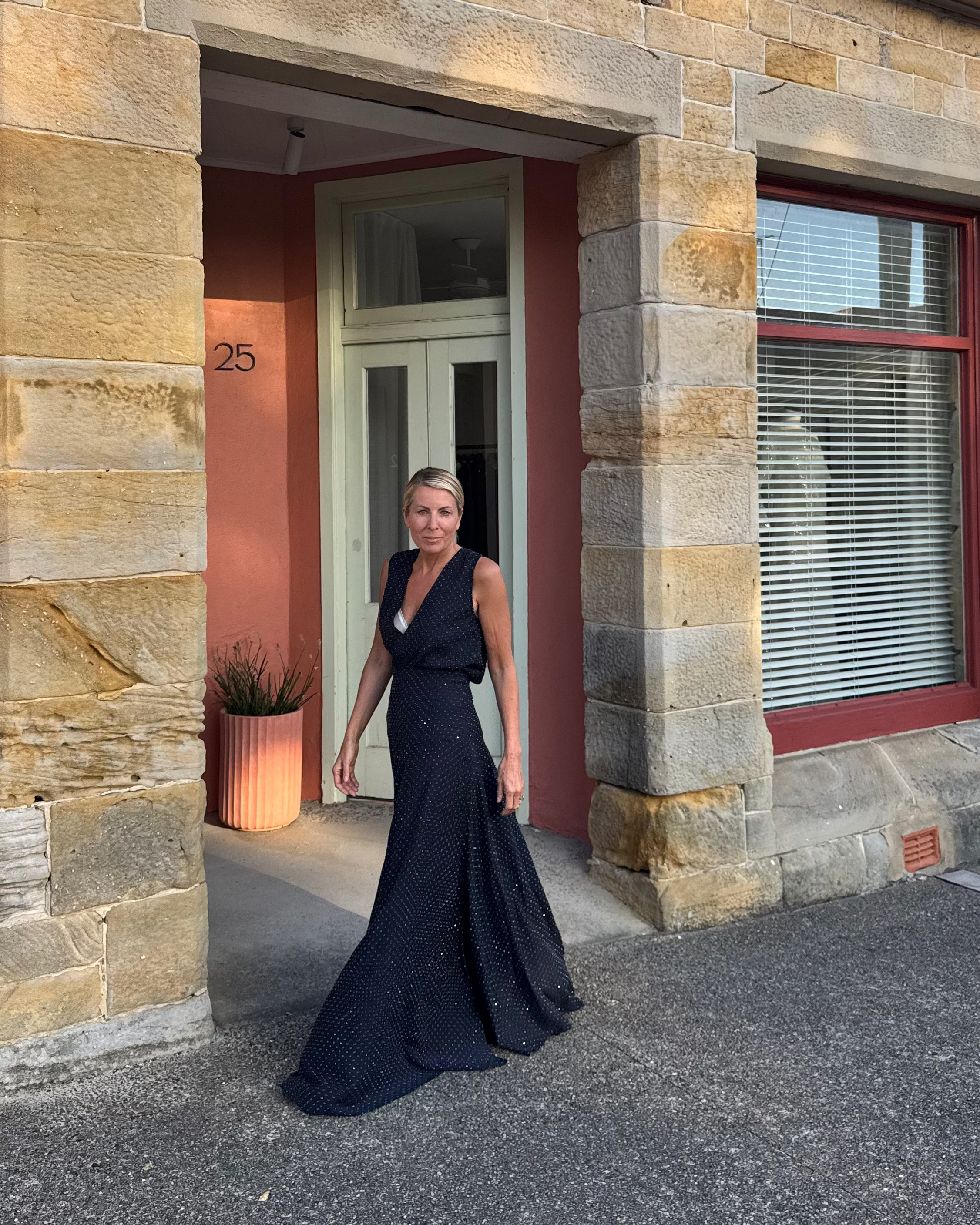 Woman in a black dress standing outside a stone building with red-framed windows.